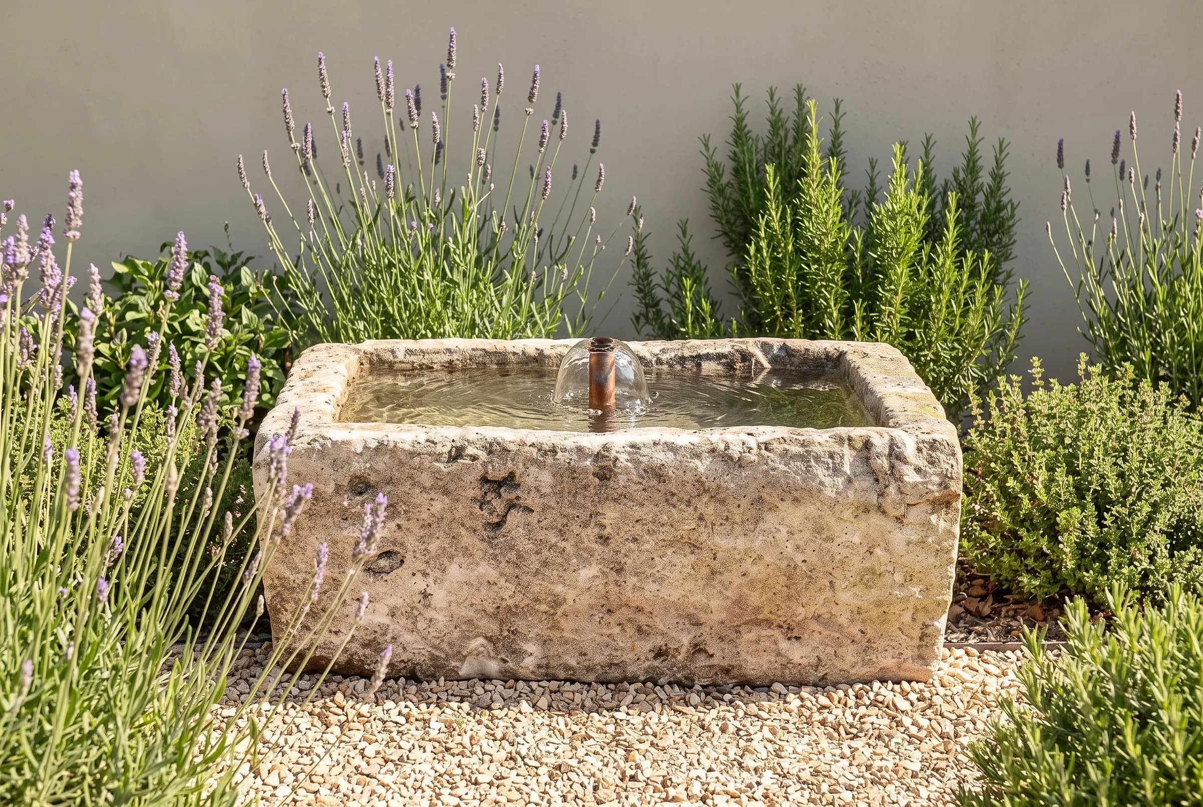 Rechthoekige natuurstenen trog als fontein tussen lavendel en rozemarijn op grind