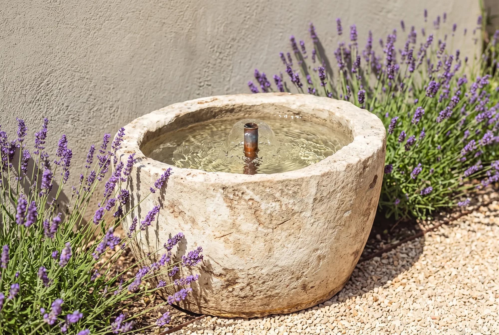 Ronde beige natuurstenen pot van Montung als fontein, met kabbelend water en koperen tuitje