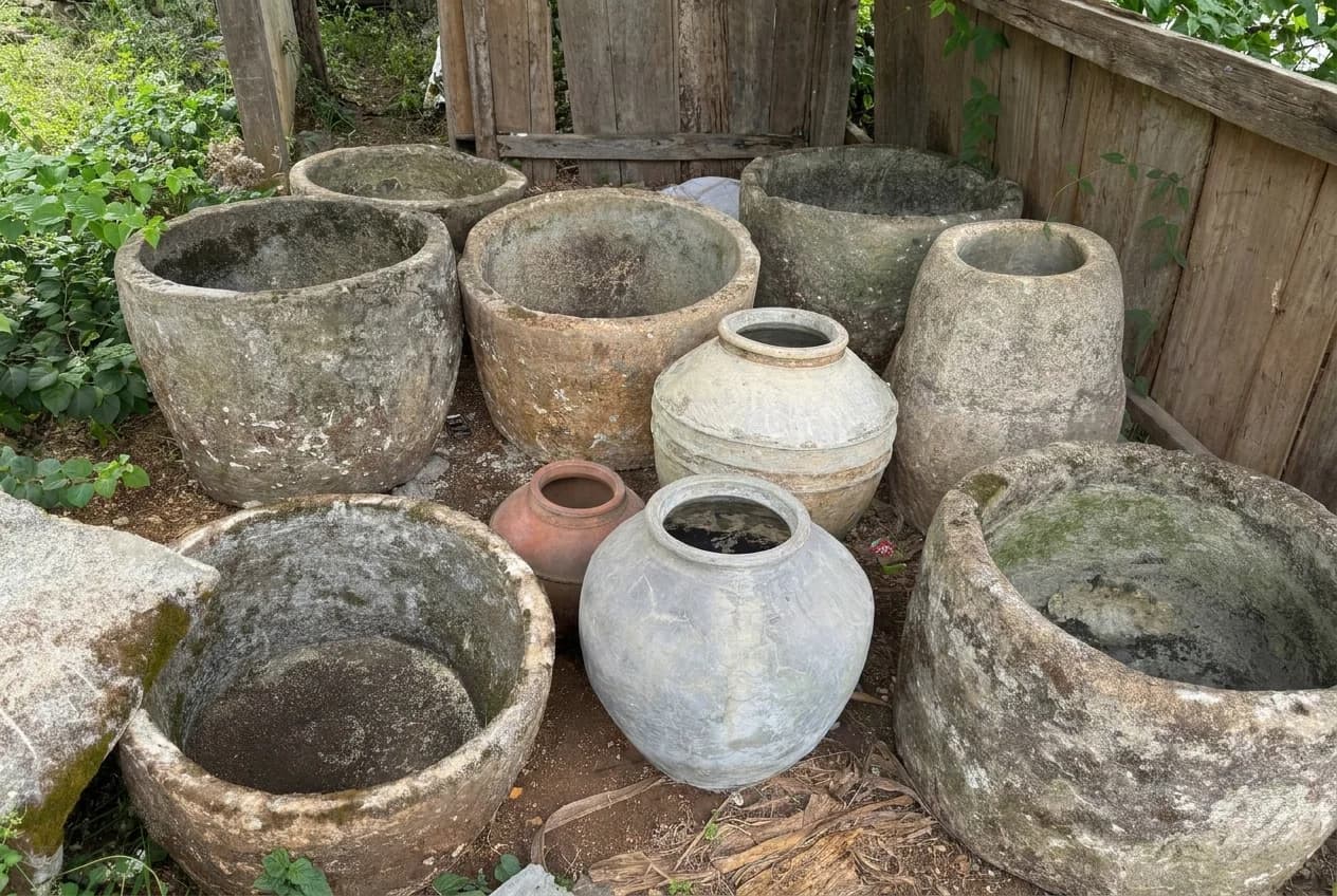 Verweerde natuurstenen potten met mos tegen een houten schutting